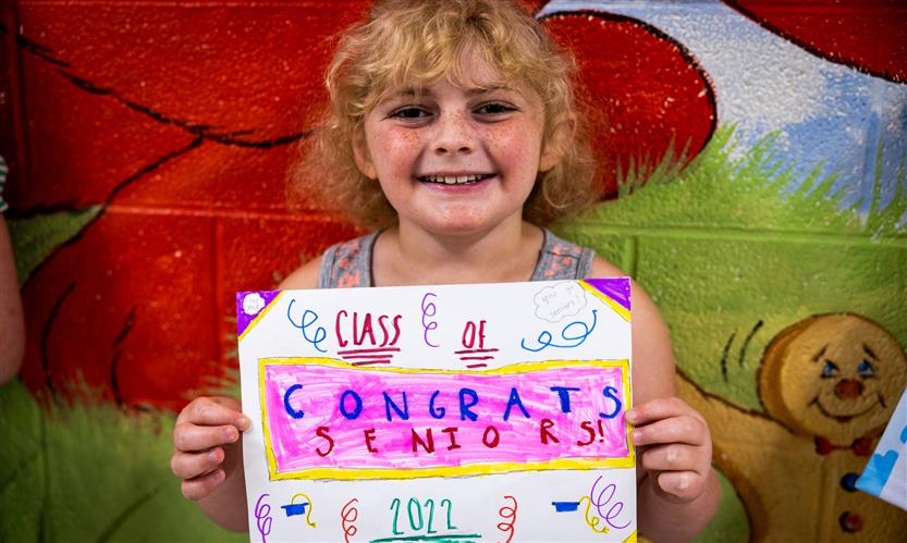 A girl holds a sign celebrating graduating seniors